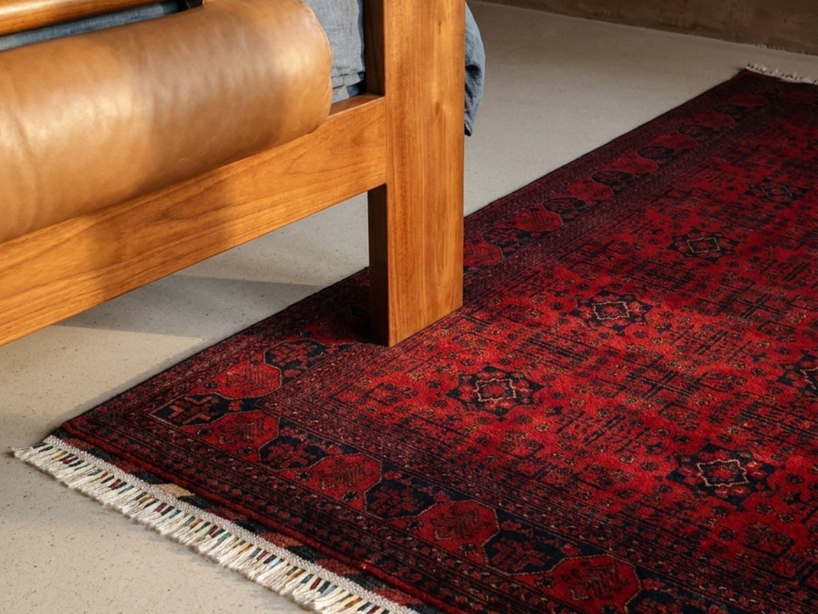A deep red rug beside a timber bed with a leather bolster