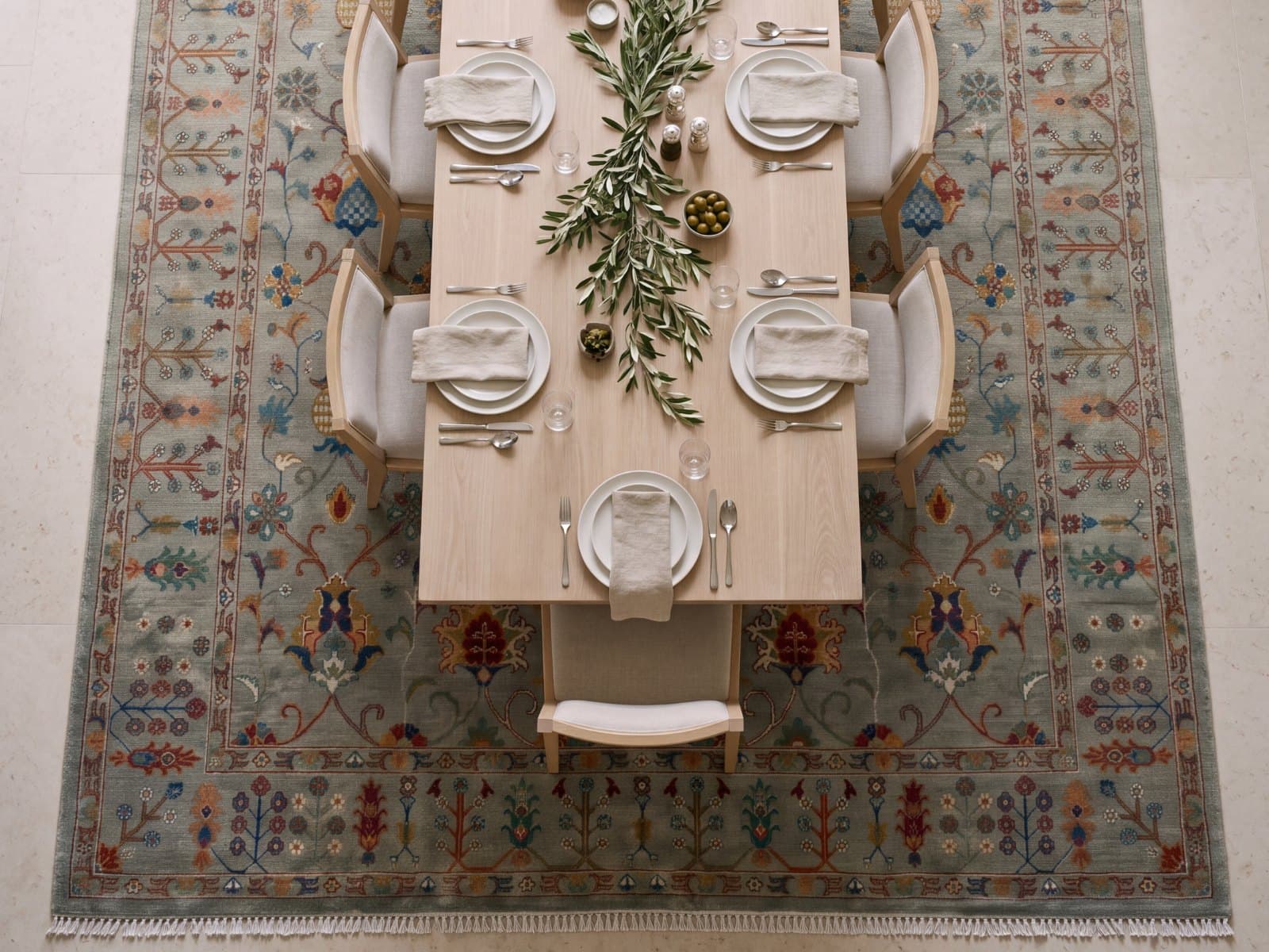 A pale blue rug beneath a laid dining table and its chairs, seen from above
